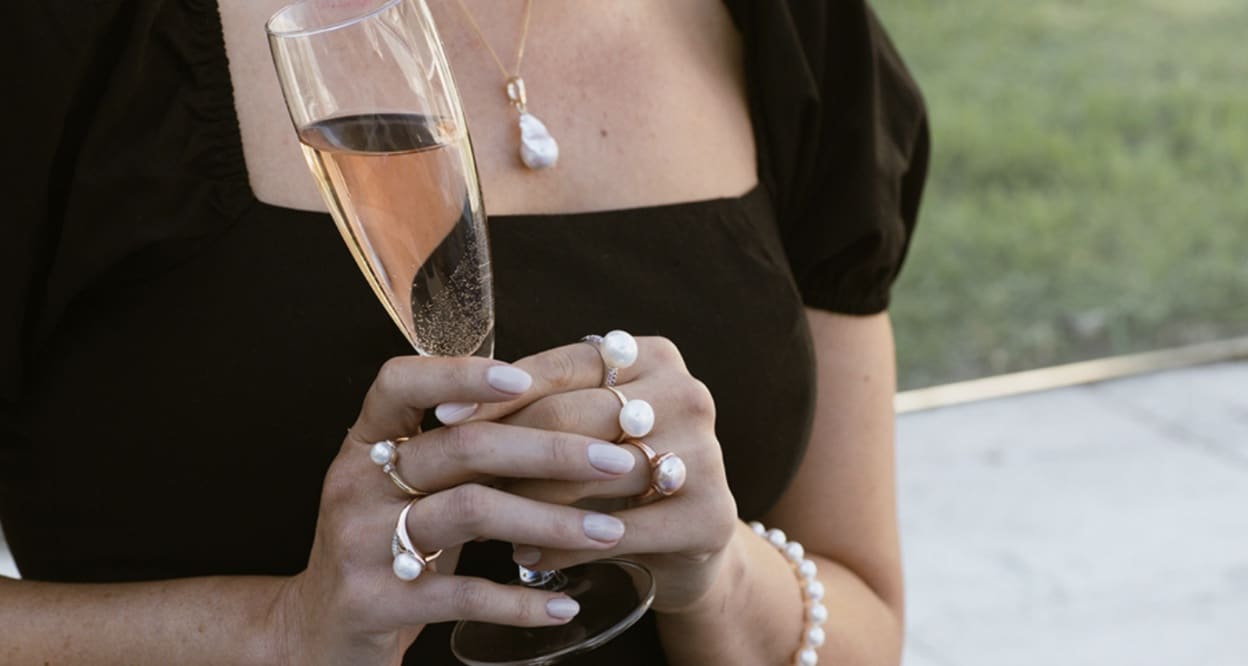 A woman dressed in a black dress holding a champagne glass and wearing Ikecho pearls